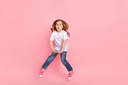 Photo of shocked funny girl jump omg reaction wear spectacles white t-shirt jeans isolated pink...