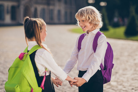 Photo of cheerful two people schoolkids hold hands look each other wear bag school uniform street outsideの写真素材