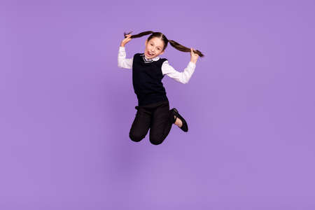 Photo of crazy childish schoolkid girl jump play ponytails show tongue wear uniform isolated violet color backgroundの写真素材