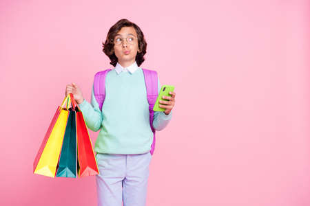 Photo of thoughtful boy hold store packages smartphone look empty space wear bag teal shirt isolated...