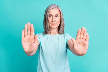 Photo of mature serious nice looking woman with short grey hair show stop sign gesture isolated on turquoise color backgroundの写真素材