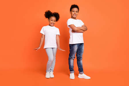 Full length photo of little cool girl boy crossed arms wear white t-shirt jeans sneakers isolated on orange backgroundの写真素材