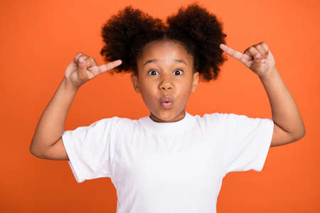 Photo of little impressed girl point hair wear white t-shirt isolated on orange color backgroundの写真素材