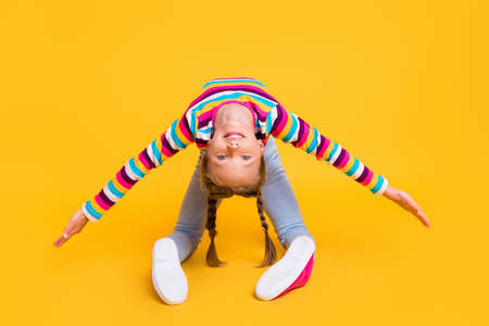 Photo of small girl stretch body care look camera wear striped shirt jeans sneakers isolated yellow color backgroundの写真素材