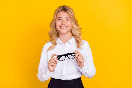 Photo of cheerful schoolgirl take off eyeglasses toothy smile wear white shirt isolated yellow color...