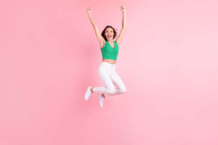 Full length body size photo smiling jumping up gesturing like winner happy overjoyed isolated pastel pink color backgroundの写真素材
