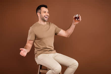 Photo portrait brunet man in pastel t-shirt drinking whiskey in bar sitting on chair isolated brown...