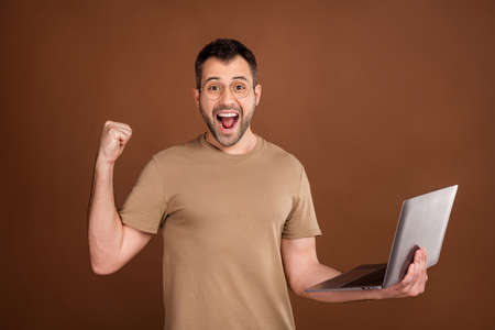 Photo of lucky pretty gentleman wear beige t-shirt spectacles holding modern gadget rising fist...