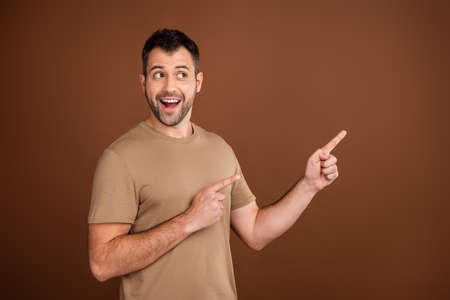 Photo of impressed cute young gentleman wear beige t-shirt pointing looking empty space smiling...