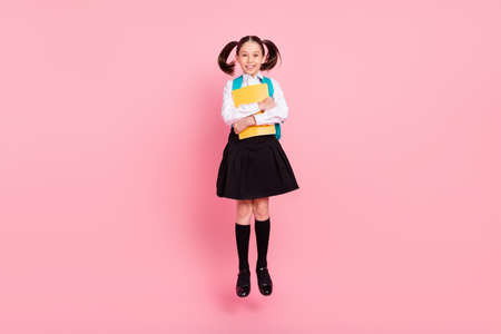 Full length photo of young happy cute small girl jump up smile hold copybooks isolated on pink color backgroundの写真素材
