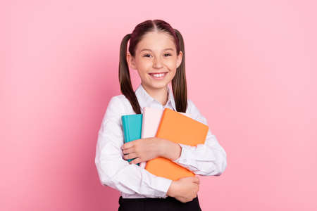 Photo of young happy positive cheerful girl hold hands hug copybooks isolated on pastel pink color backgroundの写真素材