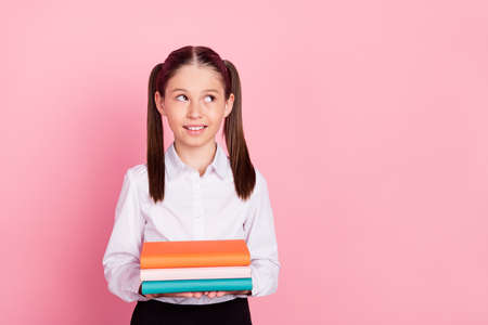 Photo of young happy small girl pupil look empty space hold hands textbooks isolated on pink color...