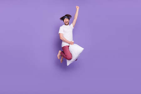 Full size portrait of carefree overjoyed person flying on cushion raise fist isolated on violet color backgroundの写真素材