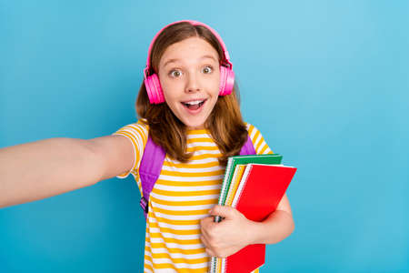 Photo of excited astonished schoolchild hold notebook recording video isolated on blue color...