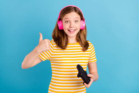 Portrait of redhair schoolgirl show thumb up wear yellow striped trendy t-shirt isolated on blue...