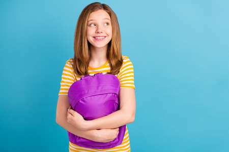 Photo of adorable positive schoolchild arms hold bag look empty space isolated on blue color backgroundの写真素材