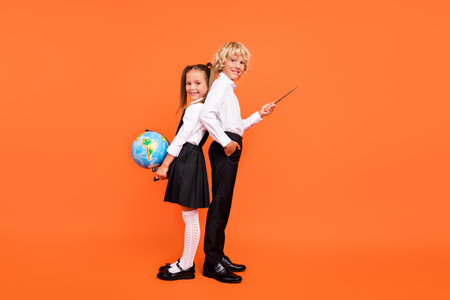Photo of two schoolkids hold globe pointer direct empty space wear uniform isolated orange color backgroundの写真素材