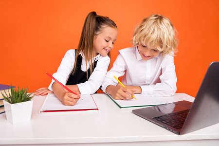 Photo of busy schoolchildren write homework desktop laptop wear uniform isolated orange color backgroundの写真素材