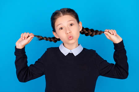 Photo of cheerful funny funky small girl hold hands braids good mood playful air kiss isolated on blue color backgroundの写真素材