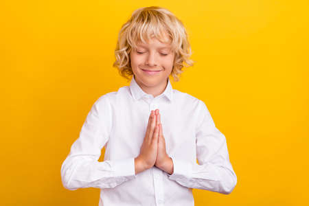 Photo of inspired schoolboy close eyes hold palms plead wear school uniform isolated yellow color backgroundの写真素材