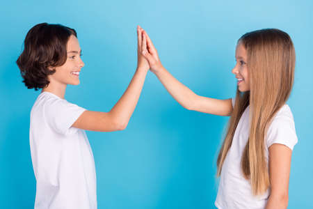 Profile photo of two teammates kids give high five victory mark wear white t-shirt isolated blue color backgroundの写真素材
