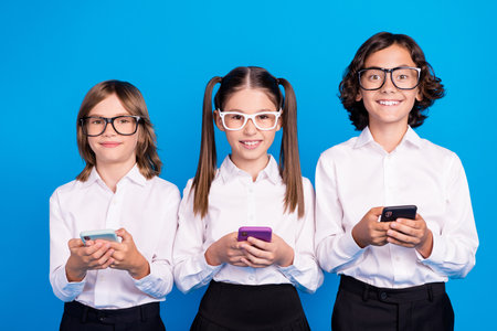 Photo of pretty charming schoolchildren wear uniform spectacles typing modern devices isolated blue color backgroundの写真素材