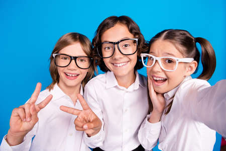 Photo of impressed funny schoolkids formalwear glasses recording video showing v-sign isolated blue color backgroundの写真素材