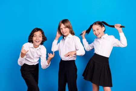 Photo of shiny carefree schoolchildren wear uniform smiling dancing showing rock sign isolated blue color backgroundの写真素材