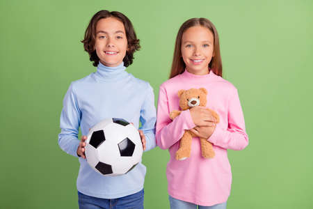 Portrait of attractive cheerful kids holding in hands toys spending free time isolated over bright green color backgroundの写真素材