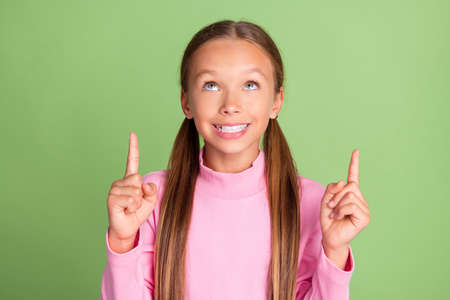 Portrait of attractive cheerful girl showing up copy space ad advert isolated over bright green color backgroundの写真素材