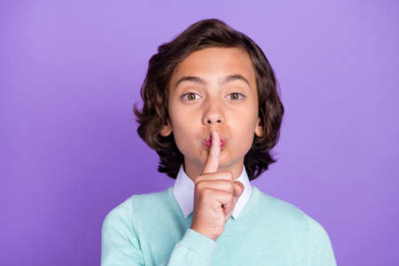 Photo of excited serious schoolboy wear teal pullover finger lips asking keep secret isolated purple color backgroundの写真素材