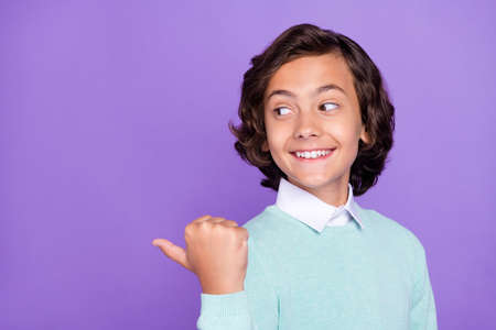 Photo of small funky brunet boy point look empty space wear blue sweater isolated on purple...
