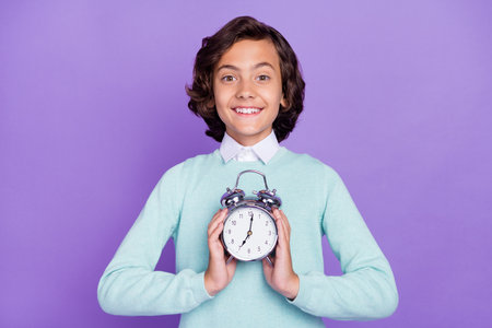 Photo of small joyful brunet boy hold clock wear blue sweater isolated on purple background
