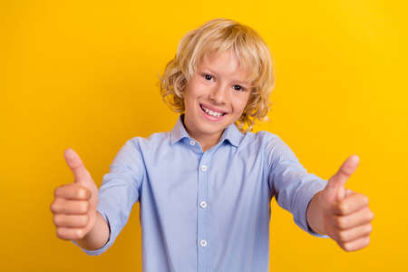 Photo of cute small boy show thumb up wear blue shirt isolated on yellow color backgroundの写真素材