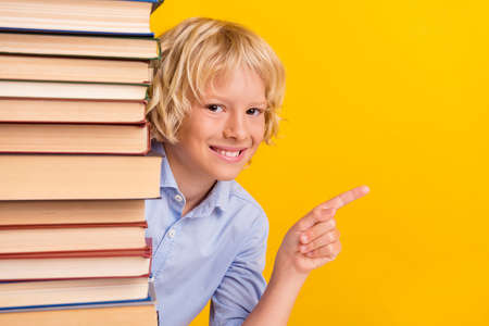 Photo of cute little boy point empty space wear blue shirt isolated on yellow color backgroundの写真素材