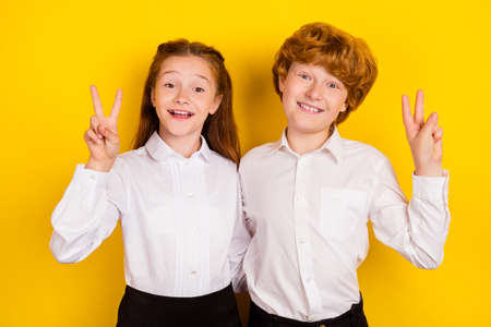 Photo of good mood positive smiling schoolchildren show v-sign back to school isolated on yellow color backgroundの写真素材