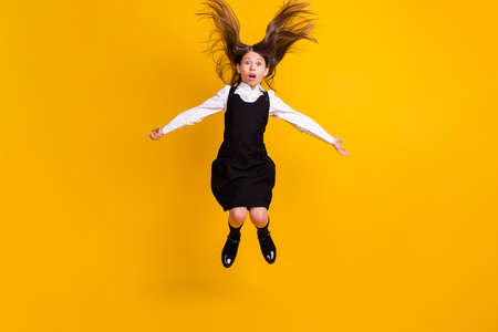 Full length photo of amazed shocked crazy girl jump up fly hair back to school isolated on yellow color backgroundの写真素材