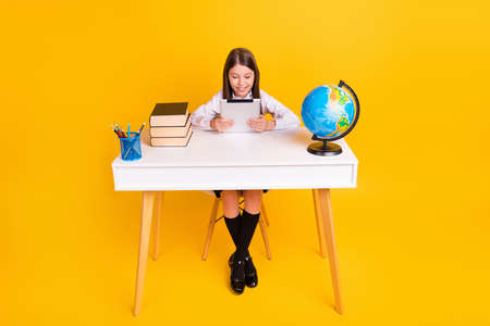 Photo portrait schoolgirl sitting at desk reading e-book on lesson isolated vivid yellow color...