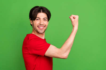 Photo of confident masculine guy show strength biceps wear red t-shirt isolated green color...
