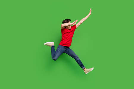 Photo of modern rave dancer guy jump make dab move wear red t-shirt jeans shoes isolated green color backgroundの写真素材