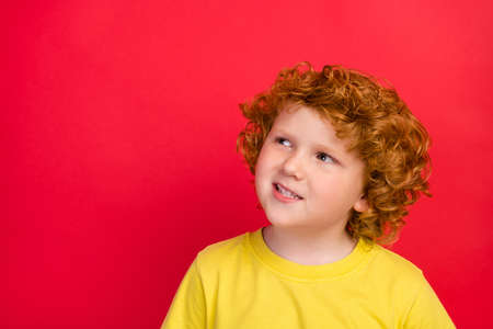 Photo of ginger dreamy inspired boy look up empty space wear yellow t-shirt isolated red color backgroundの写真素材