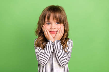 Photo of cool little blond hair girl hands cheeks wear striped shirt isolated on green color...