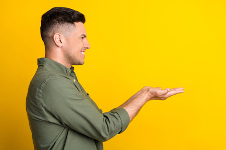 Side profile photo portrait man smiling keeping copyspace on hands isolated vivid yellow color backgroundの写真素材