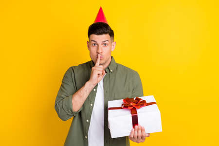 Photo of young guy cover finger lips shh keep secret surprise hold present box isolated over yellow color backgroundの写真素材