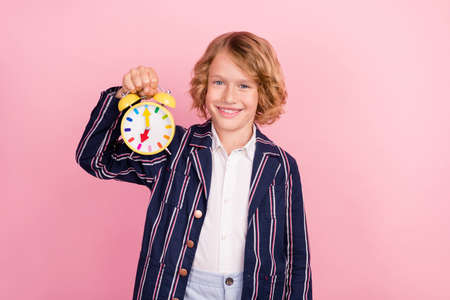 Photo of young school boy happy positive smile hold clock timer lesson study isolated over pink...