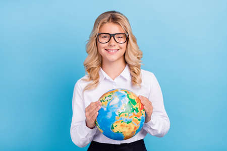 Photo of positive schoolgirl hold globe toothy beaming smile wear specs shirt isolated blue color backgroundの写真素材