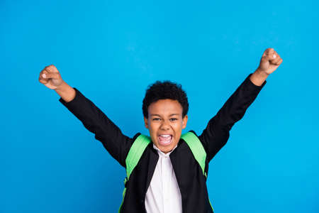 Photo of cheerful young happy positive boy raise fists winner good mood school isolated on blue color backgroundの写真素材