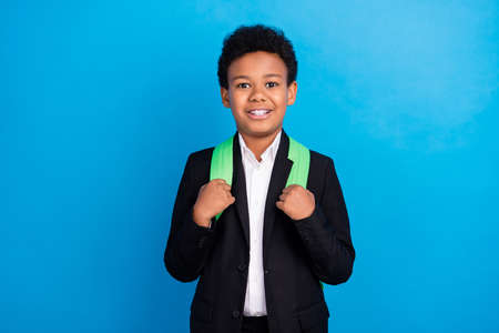 Photo of young happy positive dark skin boy good mood wear backpack smile pupil isolated on blue...