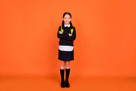 Full body photo of confident happy small girl hold hands crossed good mood supplies isolated on orange color backgroundの写真素材