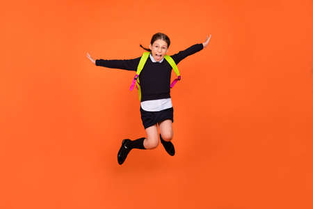 Photo of careless a-student schoolgirl jump crazy flight wear uniform backpack isolated orange color backgroundの写真素材